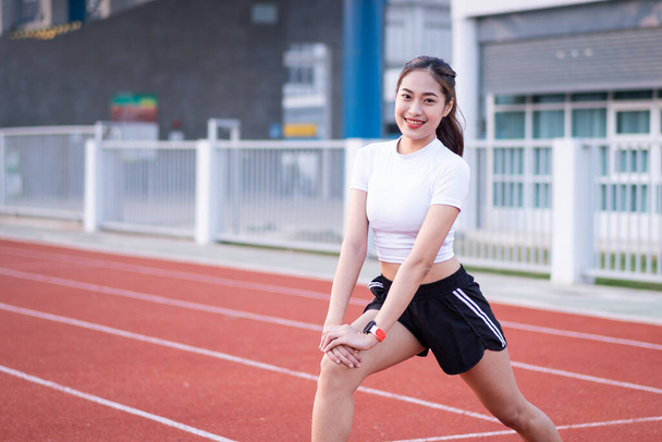 Eine junge schöne Asiatin in Sportkleidung, die morgens vor dem Training im Park Stretching macht, um einen gesunden Lebensstil zu bekommen. Gesunde junge Frau wärmt sich draußen auf - Foto, Bild