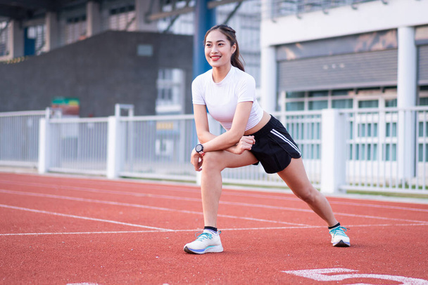 Młoda piękna Azjatka w strojach sportowych robi rozciąganie przed treningiem outdoor w parku w godzinach porannych, aby uzyskać zdrowy styl życia. Zdrowa młoda kobieta rozgrzewa się na zewnątrz - Zdjęcie, obraz