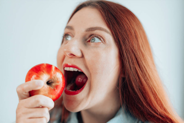 Portrait of a cheerful young woman eating red apple on gray wall background. Healthy nutrition diet. Apple vitamin snack. - Fotografie, Obrázek