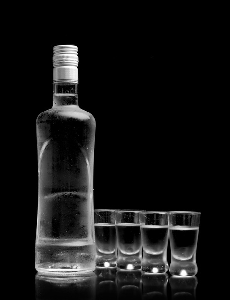 Bottle with many glasses of vodka isolated on black background - Foto, afbeelding