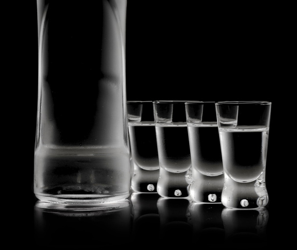 Bottle with many glasses of vodka isolated on black background - Photo, image