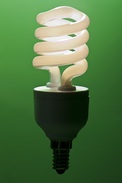 een magisch verlichte low energy light bulb tegen een groene achtergrond - Foto, afbeelding