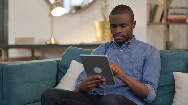 Joven africano usando tableta en sofá  - Foto, Imagen