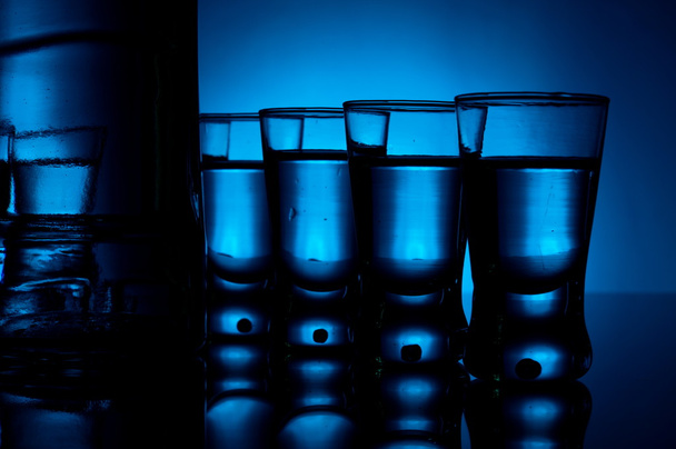 Bottle of vodka with many glasses lit with blue backlight - Foto, afbeelding