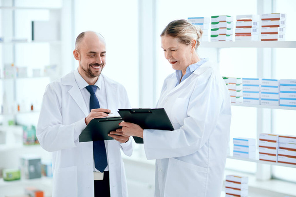smiling pharmacists discuss something standing near the shelf with medicines . - Photo, Image