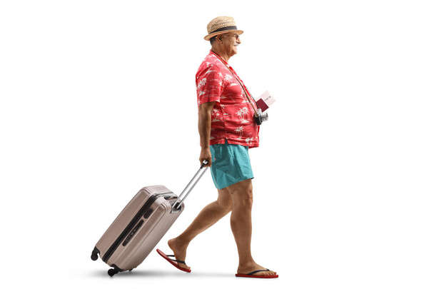 Ganzkörperaufnahme eines reifen männlichen Touristen, der einen Pass hält und einen Koffer isoliert auf weißem Hintergrund zieht - Foto, Bild