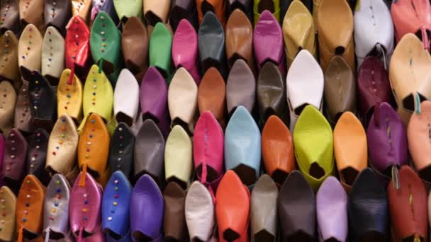 Auténticas zapatillas de colores marroquíes (babouches), expuestas en una pared, en la medina de Marrakech (Marrakech), Marruecos. Movimiento de cámara de izquierda a derecha. - Metraje, vídeo