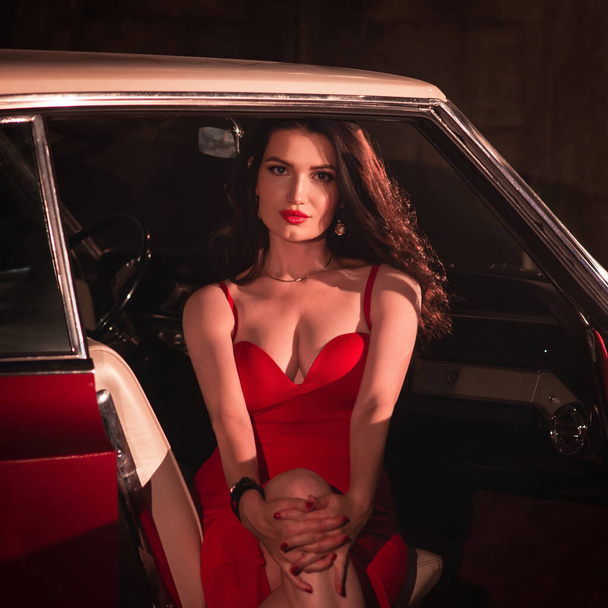 Lady, fashion model in red dress sitting in the retro car at night. - Foto, afbeelding
