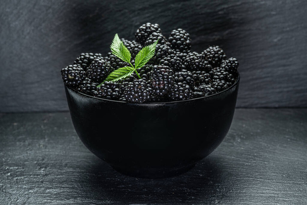 Black bowl with ripe blackberries on gray table. - Foto, afbeelding