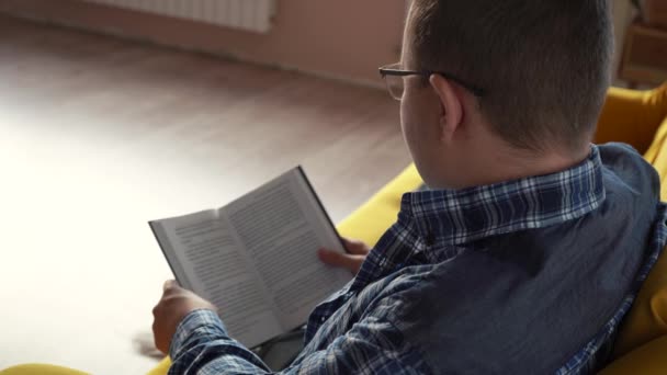 un hombre con gafas leyendo un libro acostado en el sofá - Metraje, vídeo