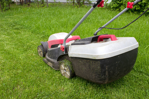 Lawn mower cutting green grass in backyard. Lawn mower on fresh green lawn. - Foto, immagini