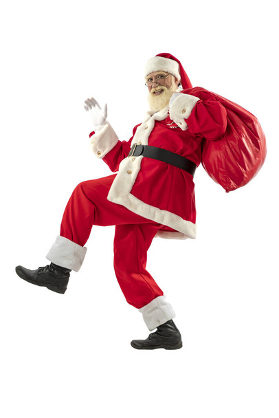 Święty Mikołaj na białym tle odizolowany. starszy męski aktor starzec z prawdziwą białą brodą w roli ojca Bożego Narodzenia trzymający torbę prezentów, biegający lub tańczący. - Zdjęcie, obraz