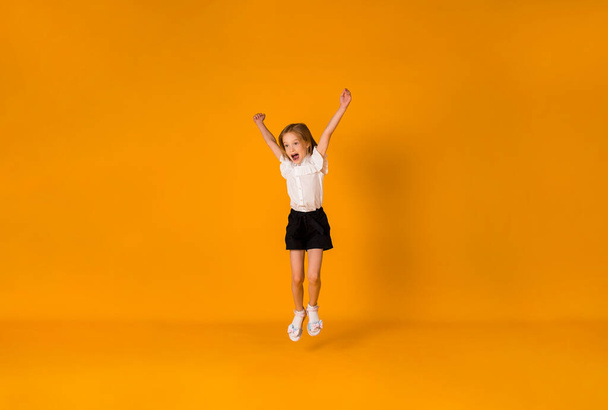 glückliches blondes Schulmädchen in Uniform springt auf einem gelben Hintergrund mit einer Kopie des Raumes - Foto, Bild