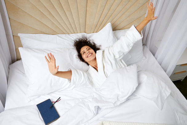 Young smiling Woman Waking Up In Bed And Stretching Her Arms Up, concept of happy beginning of the day - Photo, Image