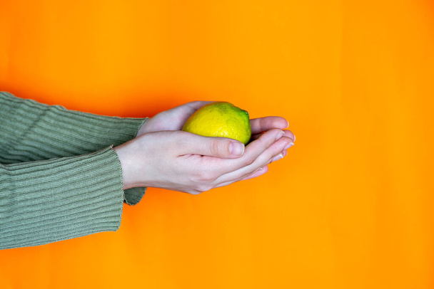 manos sosteniendo limón con fondo naranja - Foto, Imagen