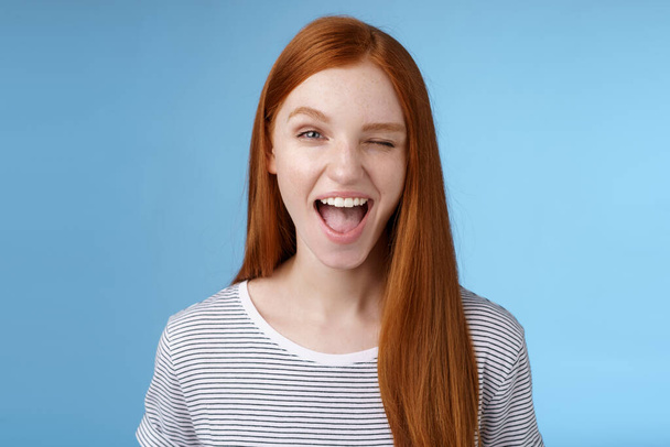 Cheeky good-looking flirty young gorgeous redhead girlfriend winking sassy smiling delighted open mouth hinting have interesting suggestion keep secret standing amused blue background - 写真・画像