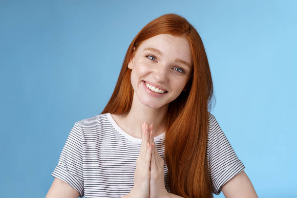 Cheerful sincere kind redhead girl do coquettish eyes tilting head look nice asking favour say please smiling tender press palms together supplicating pleading begging help, standing blue background - Photo, Image