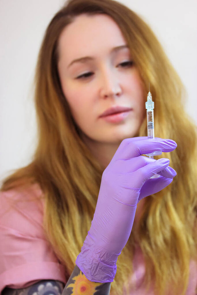 Eine junge Ärztin mit lila Gummihandschuhen hält eine Spritze mit einer dünnen Nadel in der Hand. Lippenvergrößerung, Gesichts-, Körperverjüngung, Mesotherapie. Ästhetische Kosmetologie. Schönheitssalon - Foto, Bild