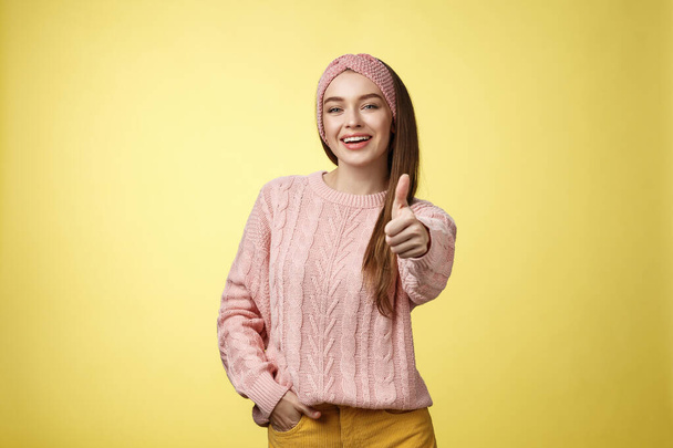 Gestures, emotions and lifestlyle concept. Self-assured positive 20s european woman wearing casual sweater over yellow background showing thumb up gesture, approving, accepting and liking concept - Photo, Image