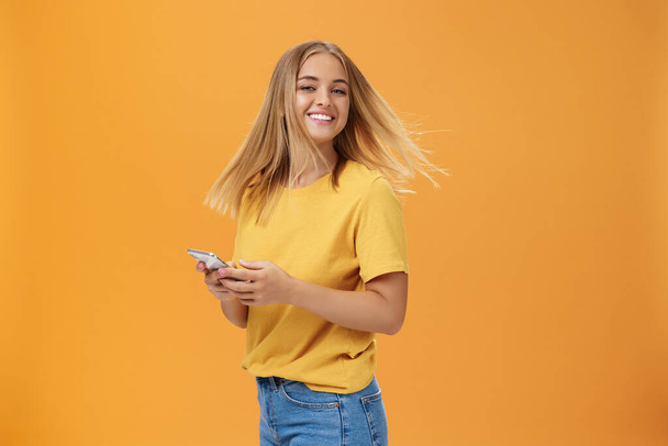 Girl feeling happy receiving message from him. Portrait of carefree charming woman with new haircut waving head standing half-turned, turning to camera with pleased cute smile holding smartphone - Zdjęcie, obraz
