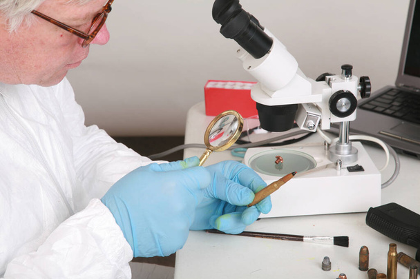Forensics. Forensics Laboratory. forensic analysis. a forensics lab technician examines a bullet and hand gun for finger prints, blood splatter, and any other residue or evidence to be used in a court case. Police specialized taking sample for exam.  - Photo, Image