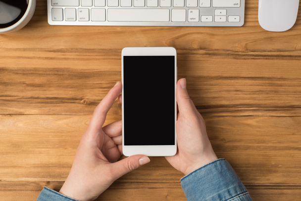 První osoba horní pohled fotografie rukou držící smartphone pohár bílá klávesnice a myš na izolovaném dřevěném stole pozadí s copyspace - Fotografie, Obrázek