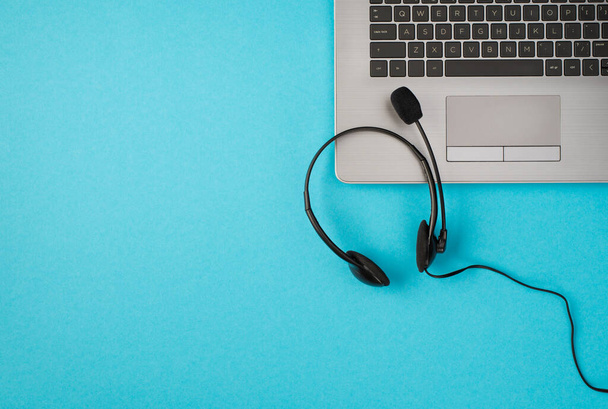 Bovenaanzicht foto van koptelefoon met microfoon op laptop op geïsoleerde pastelblauwe achtergrond met kopieerruimte - Foto, afbeelding