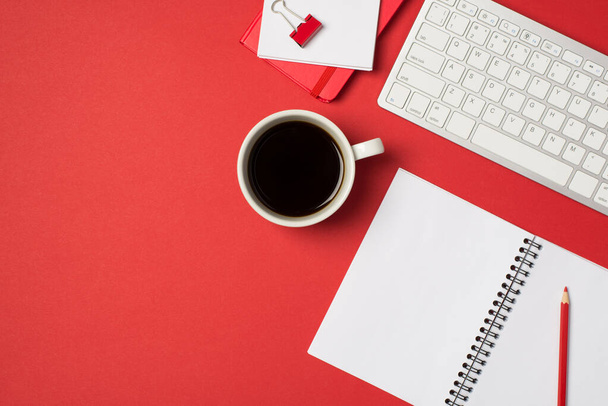 Bovenaanzicht foto van werkplek wit toetsenbord rood bindmiddel potlood organisatoren en kopje koffie op geïsoleerde rode achtergrond met copyspace - Foto, afbeelding