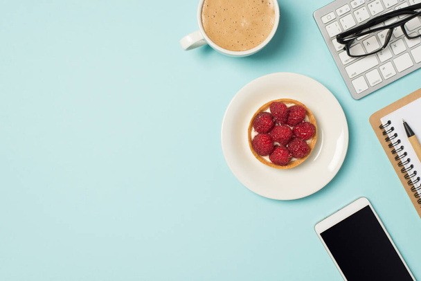 Фото бокалов на пластине планировщика клавиатуры с малиновым кексом и чашкой пенного кофе на изолированном пастельно-голубом фоне с пустым пространством - Фото, изображение