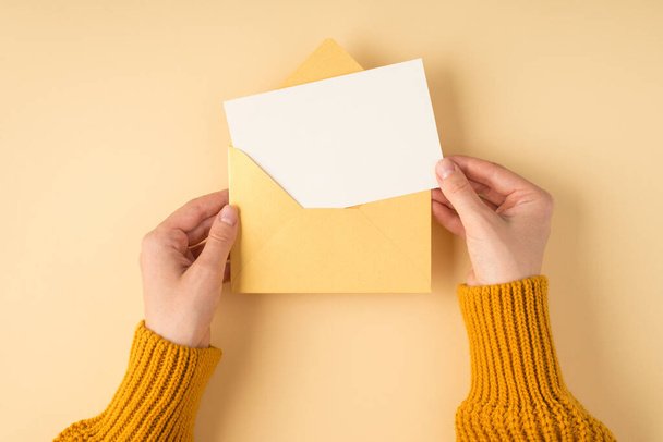 Ensimmäinen henkilö ylhäältä näkymä kuva naisten kädet keltainen villapaita tilalla avoin pastelli keltainen kirjekuori valkoinen kortti eristetty vaalean oranssi tausta kopioida - Valokuva, kuva