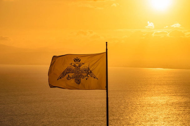 A bizánci birodalmi zászló a Messeniai-öböl felett lengedezik a sárga égbolton naplementekor. A kétfejű sas az Empire koncepciójához kapcsolódik.. - Fotó, kép