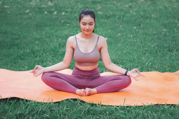 Mujer asiática practicando yoga en Root Bond, Mula Bandha posando sobre la alfombra en el parque al aire libre. - Foto, Imagen