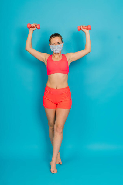 Женщина в защитной маске и спортивной одежде изолированы на синем фоне. - Фото, изображение