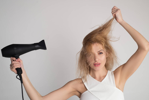 Woman touching her hair. Girl with blonde hair using hairdryer. Hairstyle, hairdressing concept. - Fotó, kép