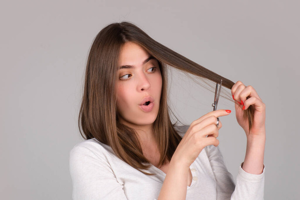 Funny woman with scissors having hair cut. Beautiful girl with straight hair with professional scissor. Haircare concept. - 写真・画像