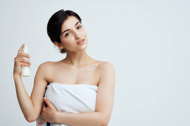 brunette with bare shoulders lotion in hand moisturizing clean skin - Foto, Imagem