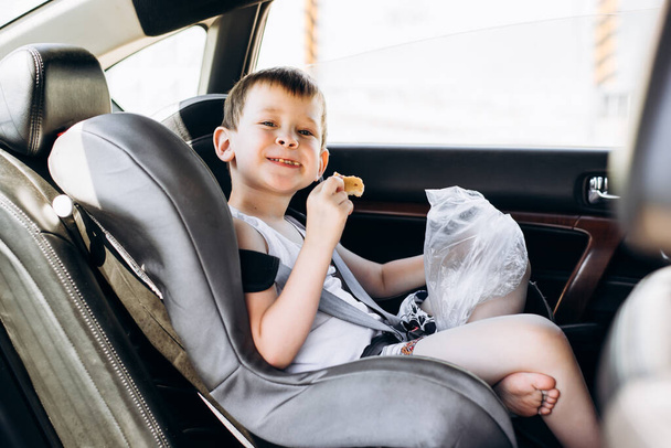 Child sitting in a car seat and eating bread. Funny little boy with a blurred face looking at the camera. - Fotoğraf, Görsel