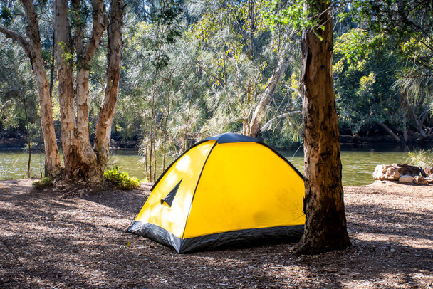 Tienda amarilla en el camping que rodea la naturaleza en la orilla del río. Camping y recreación - Foto, imagen