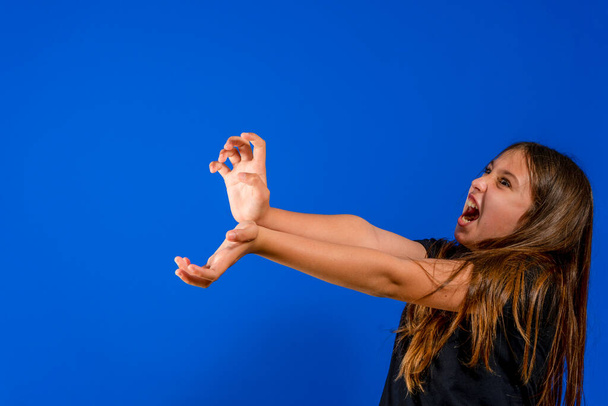 Pretty preteen girl throwing an imaginary kame kame ha with a lot of anger to win the fight isolated on blue studio background. Fun concept - Photo, Image