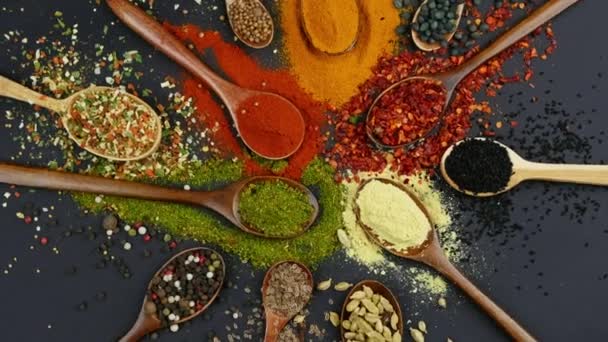 Kuivat värikkäät mausteet lusikoissa ja kulhoissa tuoreella mausteella tummalla pohjalla, ylhäältä - Materiaali, video