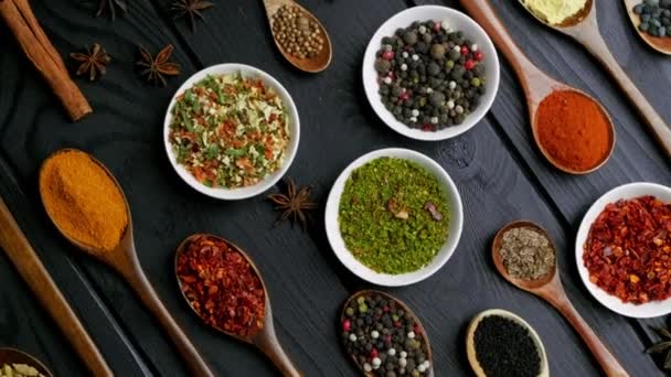 Dry colorful spices in spoons and bowls with fresh seasoning on dark background, top view - Footage, Video