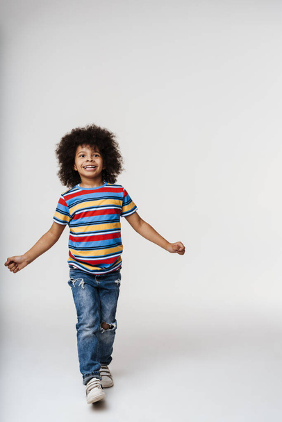 Smiling little african boy in everyday clothes over wall background, dancing - Foto, immagini