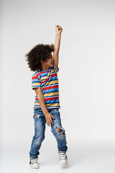 Smiling little african boy in everyday clothes over wall background, dancing - Foto, Imagen