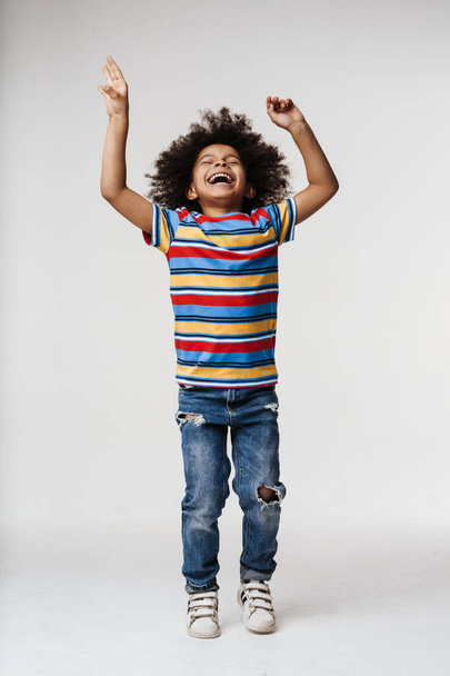 Smiling little african boy in everyday clothes over wall background, dancing - Foto, imagen