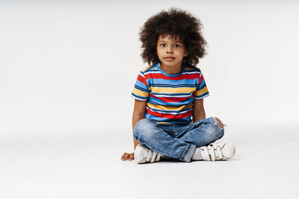 Little african boy in everyday clothes over wall background, sitting on a floor - Foto, immagini