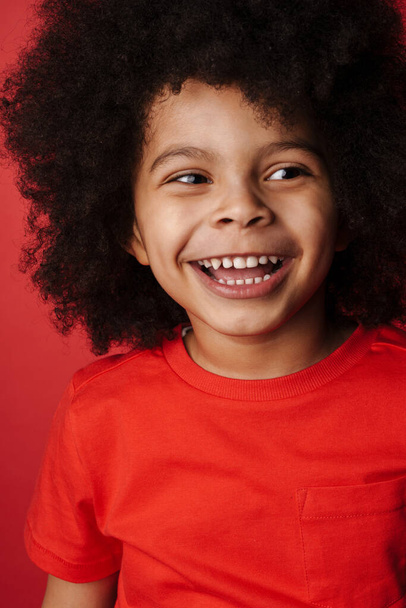 Smiling little african boy in everyday clothes over red wall background, laughing - Fotografie, Obrázek