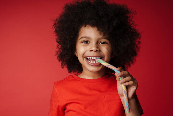 Close up of a happy african little kid eating cotton candy over red background - Photo, image