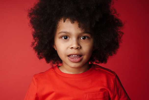 Smiling little african boy in everyday clothes over red wall background, looking at camera - Фото, зображення