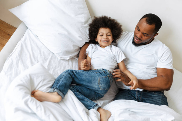Black father and son laughing while making fun in bed at home - Photo, Image