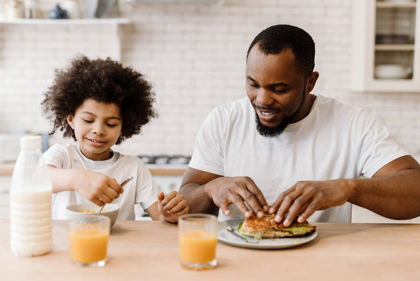 Black father and son smiling while having breakfast at home - Zdjęcie, obraz